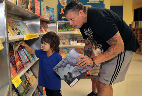 Kru Gowen, 4, and his father, Nathan Gowen, search the shelves for just the right books Sept. 4 at the Hollywood Preschool Scholastic Book Fair. Kru and his sister Irie went home with arms full of treasured new books.