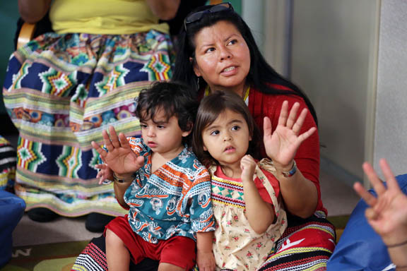 Language enrichment teacher Janelle Robinson, with her grandchildren Chaeyton Apelahoyet Robinson and Gracie Kise Robinson in her lap, raises her hands Oct. 14 to illustrate the numbers being sung in Creek in the video ‘Ten Little Indians’ at the Creek Language Enrichment House at Pemayetv Emahakv Charter School in Brighton. 
