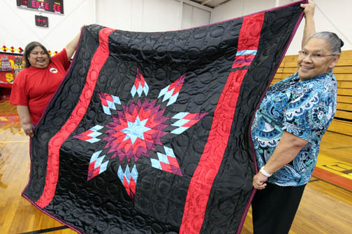 Wanda Bowers, right, and Gloria Wilson, two of the Native Relief Foundation leaders, show off one of two intricate homemade quilts up for raffle to help raise funds for the organization dedicated to providing clothes, shoes, food and toys to desolate and poor reservation communities in the cold upper Midwest. 
