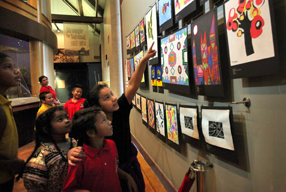 Ahfachkee School student Lauren Doctor shows younger children their artwork on exhibit in the Mosaic Gallery at Ah-Tah-Thi-Ki Museum in Big Cypress. The 26 pieces will be on display through May 22.