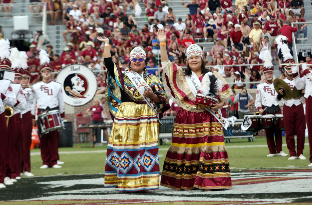 Flanked by the Marching Chiefs, Jr. Miss Florida Seminole Thomlynn Billie, left, and Miss Florida Seminole Kirsten Doney wave to the crowd Oct. 15 as they walk onto the field to crown Florida State’s homecoming chief and princess during halftime at Doak Campbell Stadium.