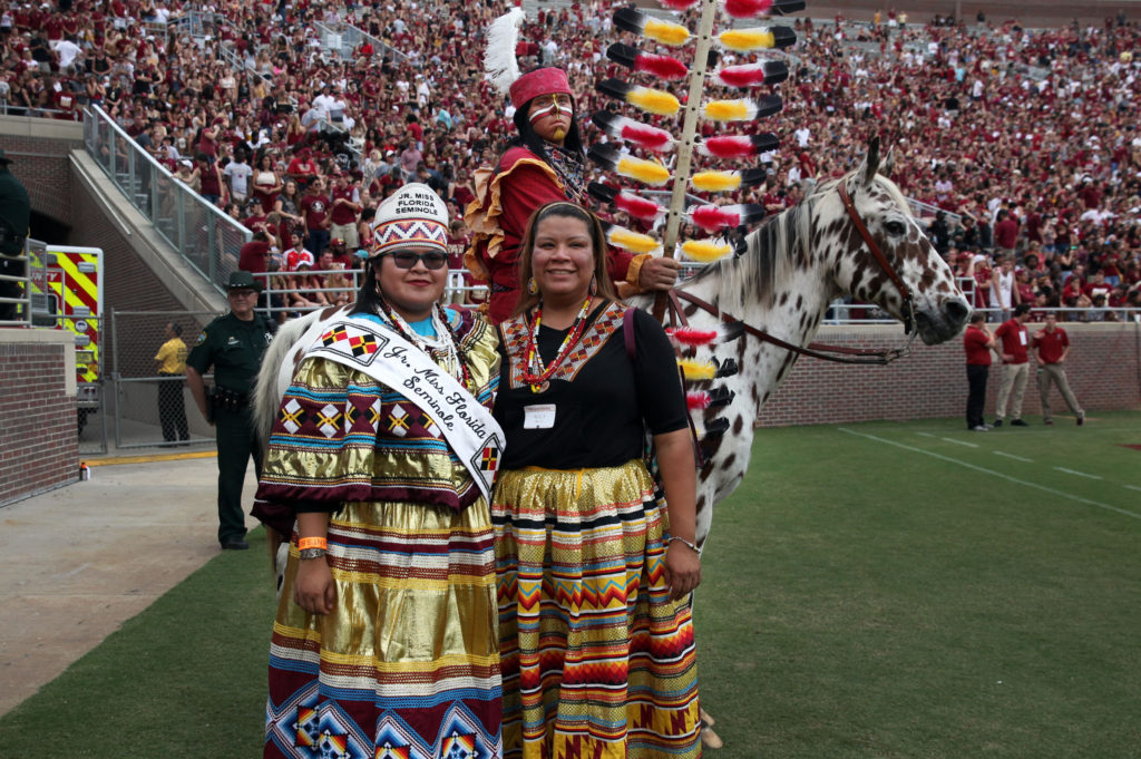 Jr. Miss Florida Seminole Thomlynn Billie and her sister Alice Billie pose with Osceola and Renegade during FSU’s homecoming game. 