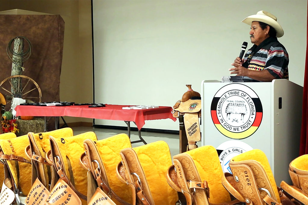 With a row of prizes for champions in front of him, Moses Jumper Jr. addresses the audience at the Easttern Indian Rodeo Association banquet in October. (Carlos Fuentes photo)