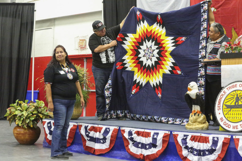 Hollywood Board Rep. Steve Osceola and Master of Ceremonies Junior Battiest and present U.S. Navy veteran Salli Josh with a blanket especially designed and created by Seminole women for the Veterans Day celebration. (Stephanie Rodriguez photo)