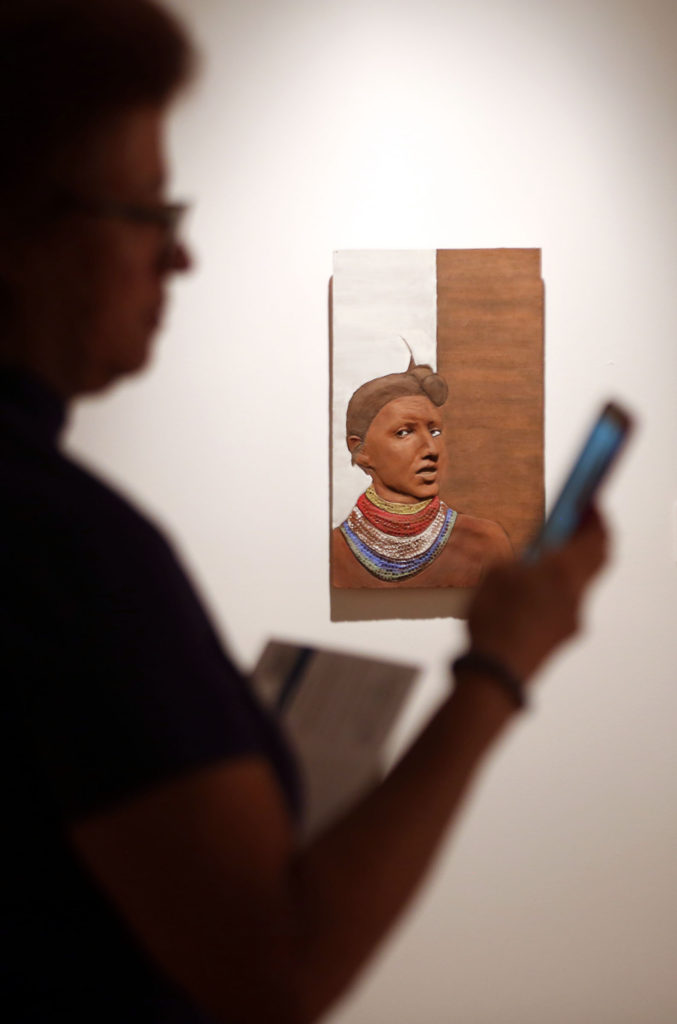 One of Jessica Osceola’s ceramic bas-relief sculptures, part of her Master of Fine Arts thesis exhibition at Florida Gulf Coast University’s ArtLab Gallery, appears to have an opinion about this art patron’s use of a cell phone in the gallery Dec. 8. (Beverly Bidney photo)