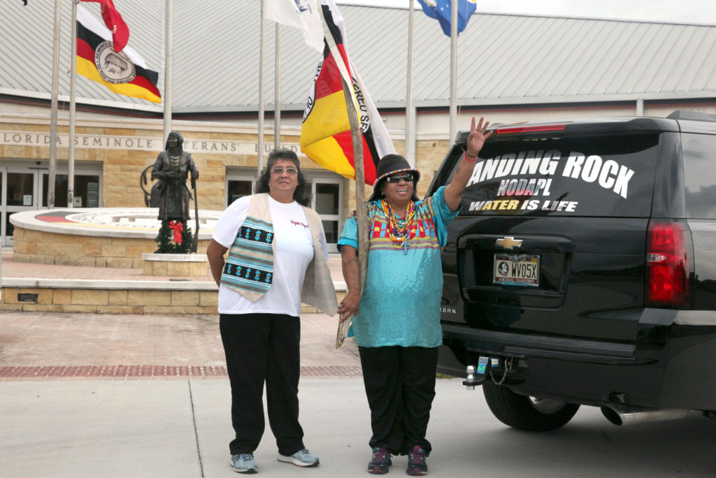 Beverly Bidney Annette Jones and Martha Tommie wave to passersby in front of the Veterans Building in Brighton on Dec. 6. Tommie put the windshield sign supporting Standing Rock’s protest against DAPL when she returned from North Dakota in September. (Beverly Bidney photo)
