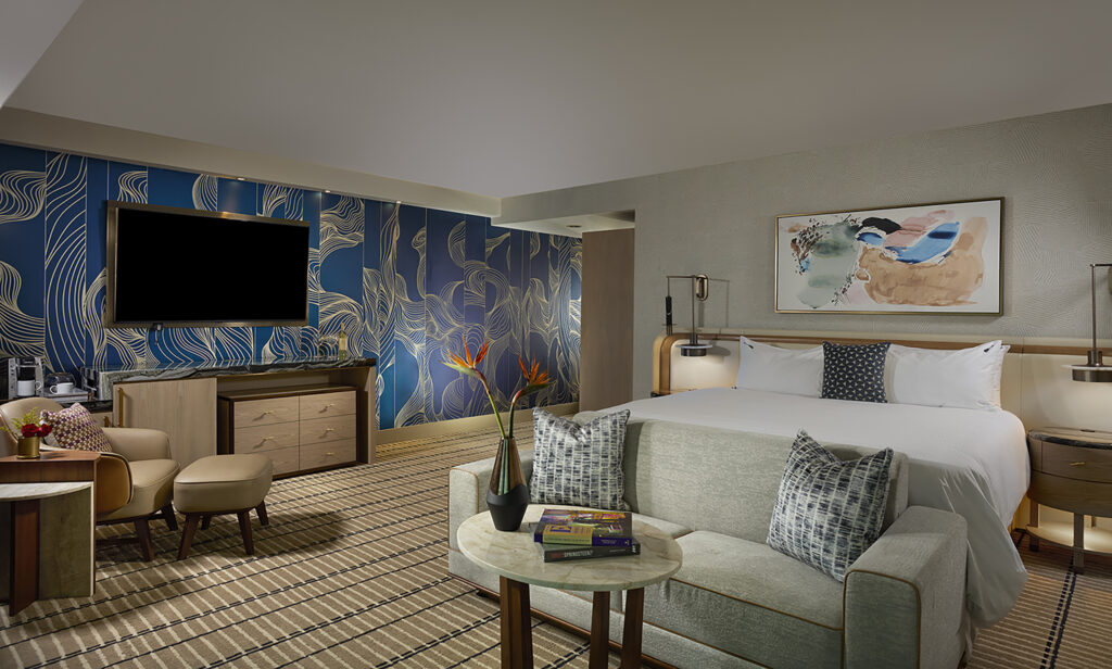 A recently renovated luxury king guest room at Seminole Hard Rock Hotel & Casino Tampa. There is a king bed with white sheets and a grey couch at the foot of the bed.