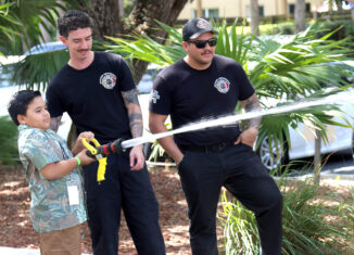 Royce Ramos uses a Seminole Fire Rescue fire hose during the hose cone knockdown challenge assisted by Seminole Fire Rescue Firefighter Adel Diaz and Fire Rescue Lieutenant Elvis Hernandez at the Take Your Child to Work Day event.