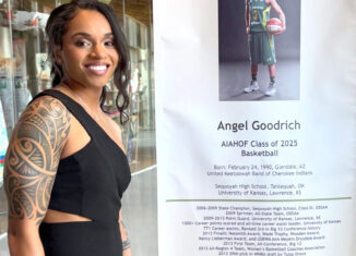 Angel Goodrich attends the National American Indigenous Athletics Hall of Fame ceremony. Goodrich stands next to a "Hall of Fame" sign.