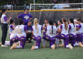 Okeechobee coaches Danny Bonilla and Mary Huff speak to the team after its 4-2 loss. The team, in purple and white uniforms, take a knee in a circle around the coaches.